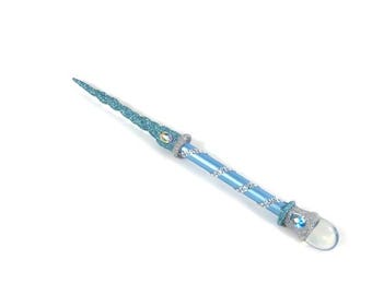 May include: A light blue and silver fantasy wand with a glittery, pointed tip. The wand has a light blue shaft with silver accents and is adorned with clear and blue gemstones. The wand is designed for fantasy play or costume use.