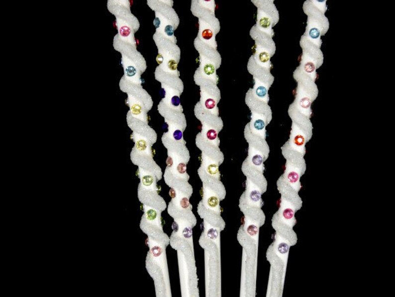 May include: Five white, twisted, decorative sticks with colorful beads. The beads are arranged in a rainbow pattern.