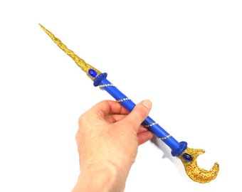 May include: A gold and blue wand with a crescent moon design at the end. The wand is decorated with blue gems and gold glitter.