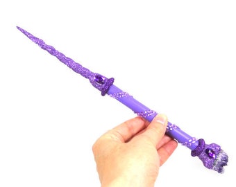 May include: A purple wand with a sparkly finish and a purple gem at the tip. The wand is decorated with purple beads and has a spiral design.