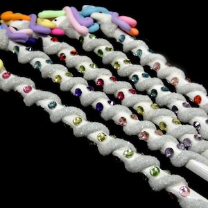 May include: A set of six white unicorn pencils with glitter and colorful rhinestones. The pencils are decorated with pastel-colored unicorn heads.