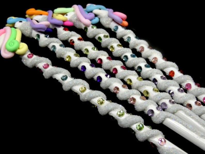 May include: A set of six white unicorn pencils with glitter and colorful rhinestones. The pencils are decorated with pastel-colored unicorn heads.
