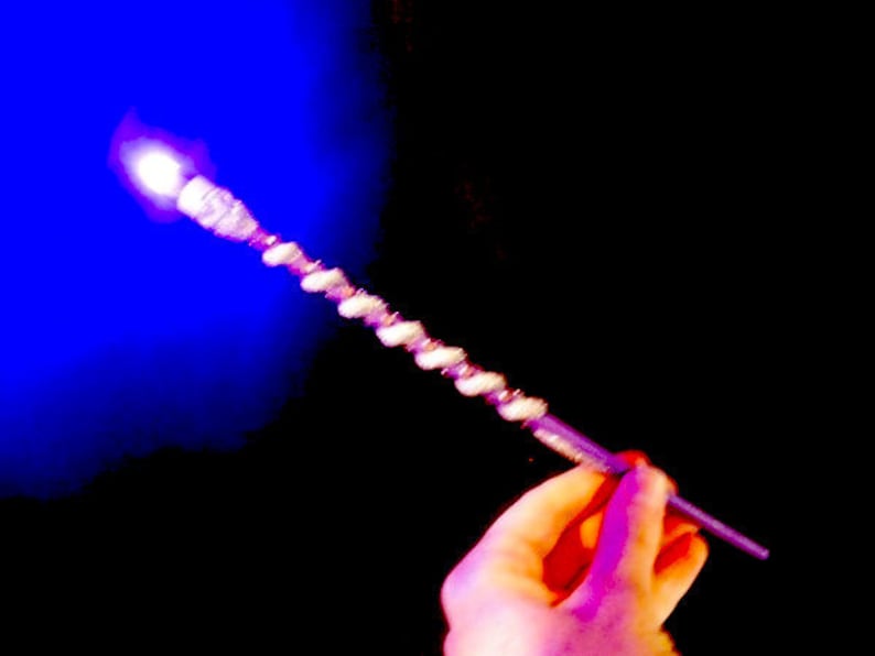 May include: A silver wand with a sparkly, iridescent finish. The wand is held in a hand against a dark blue and black background.