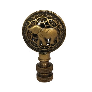 May include: A gold-toned metal lamp finial with an intricate design featuring an elephant in a circle.