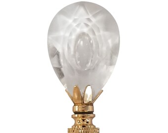 May include: A clear glass lamp finial with a faceted design and a gold metal base.