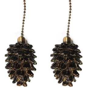 May include: Two gold-toned metal chains with pine cone-shaped ends. The pine cones are brown with a gold-toned finish.