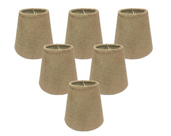 May include: A set of six small, tapered lamp shades made from a light brown, textured burlap fabric. Each shade features a simple, cylindrical shape with an open top and bottom, designed to fit over a light bulb for a soft, diffused lighting effect.