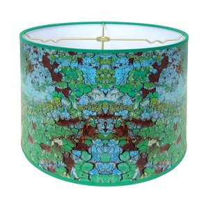 May include: A green lampshade with a distressed blue, green, and brown pattern. The lampshade has a white interior and a gold metal frame.