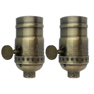 May include: Two antique brass light bulb sockets with a side switch. The sockets are labeled "250V RU1 5A LAMPH"
