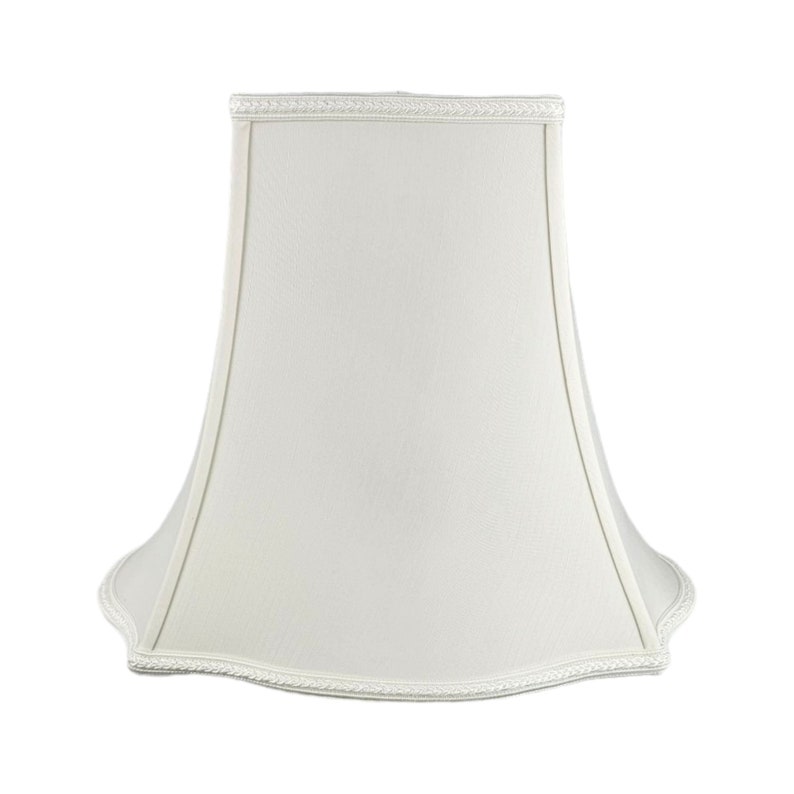 May include: A white lampshade with a scalloped edge and a white trim. The lampshade is made of fabric and has a bell shape.