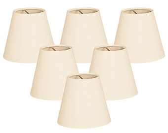 May include: Set of six off-white fabric lampshades with a simple, conical shape. The lampshades are designed for use with standard light bulbs.