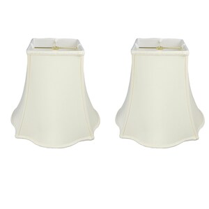 May include: A set of two off-white lampshades with a scalloped edge. The lampshades are square at the top and taper to a rounded bottom.