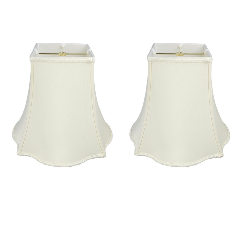 May include: A set of two off-white lampshades with a scalloped edge. The lampshades are square at the top and taper to a rounded bottom.