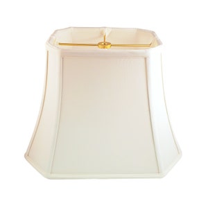 May include: A white, square-shaped lampshade with a gold metal frame. The lampshade has a slightly curved shape and a smooth, white fabric finish.