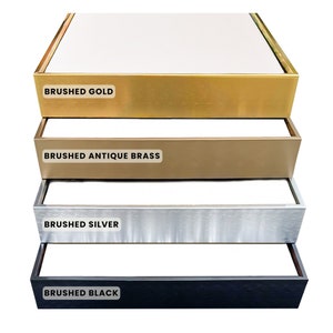 May include: Four different colored picture frames, stacked on top of each other. The frames are brushed gold, brushed antique brass, brushed silver, and brushed black.