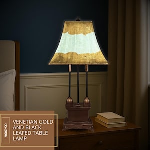 May include: Venetian gold and black leafed table lamp. The lamp features a rectangular lampshade with gold leaf accents and a light blue center. The base is brown with ornate detailing, and the lamp has three black support rods.