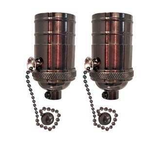 May include: Two antique bronze light bulb sockets with pull chains. Each socket has a decorative chain with a round pull.