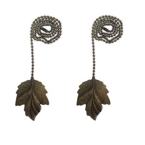 May include: Two antique gold-toned leaf-shaped pull chains for blinds or light fixtures. Each chain has a decorative leaf-shaped end and a looped chain.