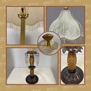 May include: A decorative table lamp with a pineapple-shaped base and a cream-colored lampshade. The base is gold and brown, with a detailed pineapple design. The lampshade has a fringe trim and a gold finial.