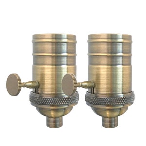 May include: Two antique brass light bulb sockets with a side switch. The sockets are made of metal and have a brushed finish.
