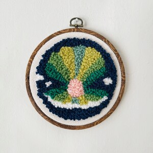 May include: A circular embroidery hoop with a colorful, abstract design in shades of green, blue, yellow, and pink. The design is created using yarn and is stitched in a circular pattern.