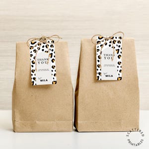 May include: Two brown paper gift bags with thank you tags tied to them. The tags are white with a black and orange leopard print and the text "Thank You for making my day so awesome from Mila".