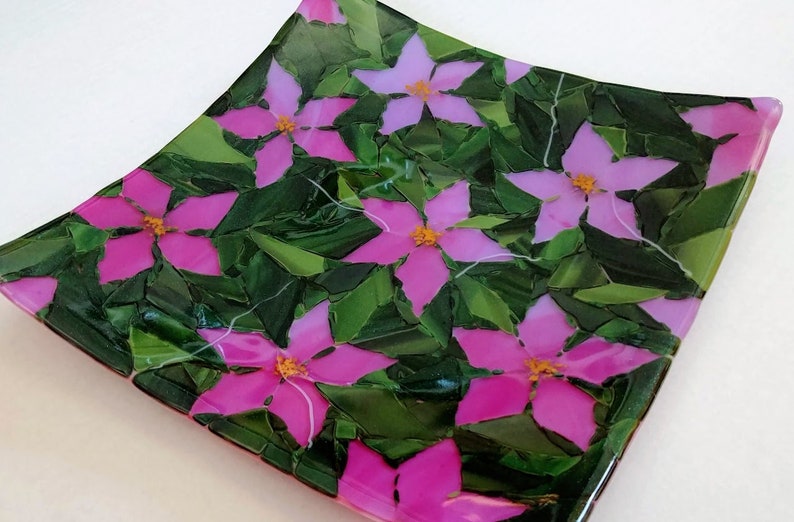 K&ouml;nnte beinhalten: Quadratische Glasplatte mit einem Mosaikdesign aus rosa Bl&uuml;ten und gr&uuml;nen Bl&auml;ttern.