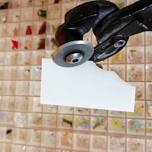 K&ouml;nnte beinhalten: Ein Glascutter mit schwarzem Griff und silbernem Rad. Das Werkzeug schneidet ein St&uuml;ck wei&szlig;es Glas.