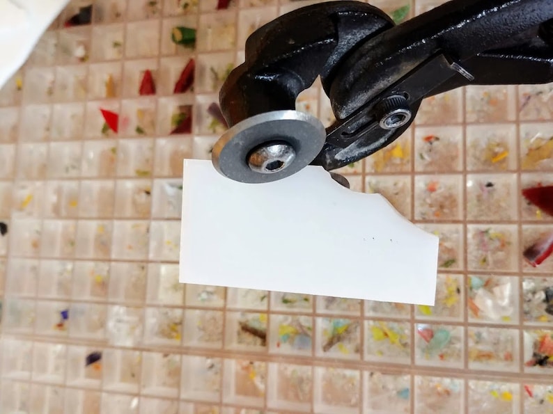 K&ouml;nnte beinhalten: Ein Glascutter mit schwarzem Griff und silbernem Rad. Das Werkzeug schneidet ein St&uuml;ck wei&szlig;es Glas.