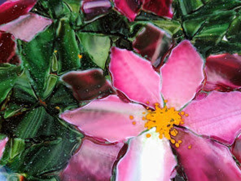 K&ouml;nnte beinhalten: Nahaufnahme einer rosa Blume mit gelber Mitte, umgeben von gr&uuml;nen Bl&auml;ttern. Die Blume ist aus Glasmosaik.
