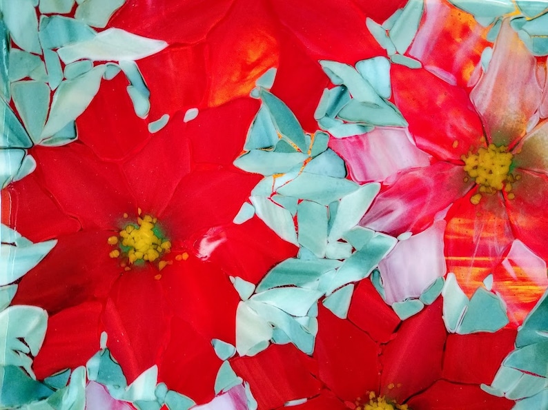 K&ouml;nnte beinhalten: Nahaufnahme eines roten, wei&szlig;en und blauen Glaskunstwerks mit einer Weihnachtsstern-Blume. Die Blume besteht aus vielen kleinen Glassplittern, die einen Mosaik-Effekt erzeugen.