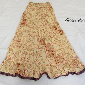 May include: A long, tiered skirt in a golden cream color featuring a repeating pattern of red and brown floral motifs and wavy lines. The skirt has an elasticized waistband and a dark purple hemline. The text Golden Color is visible.