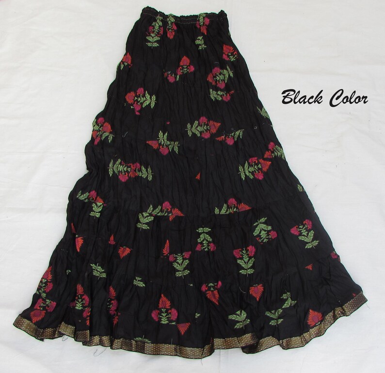 May include: A black tiered skirt featuring a crinkled texture and a repeating floral pattern in shades of red and green. The hem is finished with a metallic gold-toned border. The text "Black Color" is printed on the right side of the image.