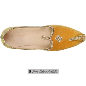May include: A mustard yellow velvet slip-on shoe featuring a pointed toe and gold-toned trim. The upper is decorated with small, clear rhinestones arranged in a diamond pattern and along the collar. The interior is lined in a light beige material.