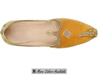 May include: A mustard yellow velvet slip-on shoe featuring a pointed toe and gold-toned trim. The upper is decorated with small, clear rhinestones arranged in a diamond pattern and along the collar. The interior is lined in a light beige material.