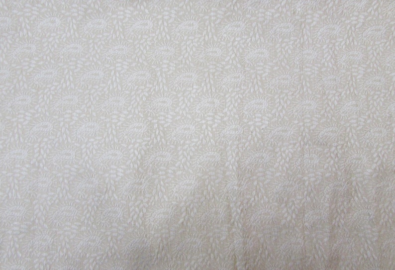 May include: Cream-colored fabric with a repeating pattern of stylized floral and leaf designs. The pattern is in a lighter shade of cream, creating a subtle contrast. The fabric appears to be a woven material.