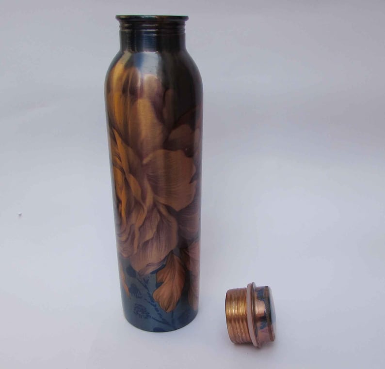 May include: A copper water bottle with a floral design in shades of brown and gold. The bottle has a matching copper cap next to it. The bottle is cylindrical and appears to be made of metal.