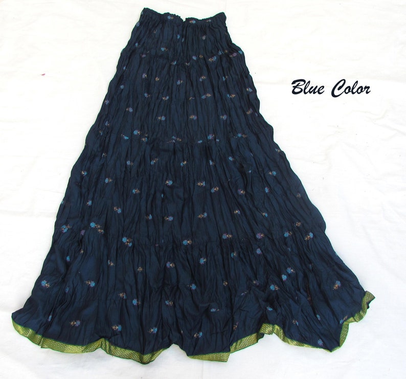 May include: A dark blue maxi skirt with a crinkled texture and a small floral pattern throughout. The skirt features an elasticized waistband and a contrasting green hem with a subtle dotted pattern. The text Blue Color is visible on the right.
