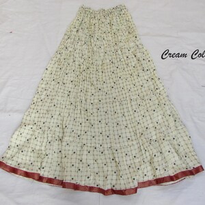 May include: A cream-colored tiered skirt featuring a repeating grid pattern with small dark circular accents. The skirt has an elasticized waistband and a wide, dark red border along the bottom hem. The text "Cream Color" is printed on the right.