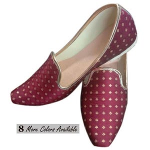 May include: A pair of maroon slip-on shoes featuring a repeating gold diamond pattern and gold trim along the edges. The interior is lined in a light beige material. A small rectangular label on the side displays the text 8 More Colors Available.