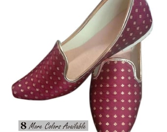 May include: A pair of maroon slip-on shoes featuring a repeating gold diamond pattern and gold trim along the edges. The interior is lined in a light beige material. A small rectangular label on the side displays the text 8 More Colors Available.