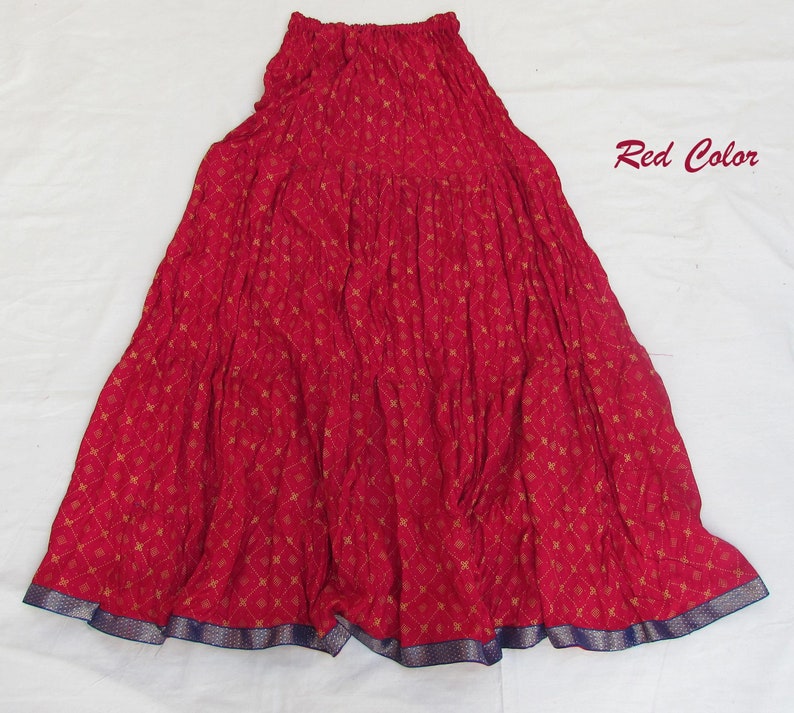 May include: A red tiered skirt featuring a repeating gold diamond and floral pattern, an elasticized waistband, and a dark blue border at the hem. The text Red Color is printed in the upper right corner of the image.