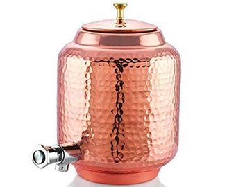 Könnte beinhalten: Ein Wasserspender aus gehämmertem Kupfer mit zylindrischem Körper, einem abnehmbaren Deckel mit kleinem goldfarbenem Knaufgriff und einem silberfarbenen Metallhahn an der unteren Vorderseite zur Entnahme von Flüssigkeit aus dem Behälter.