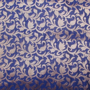 May include: A deep blue fabric featuring a repeating woven pattern of light beige floral and leaf motifs. The design consists of stylized tulip-like shapes and swirling vines that create a dense, intricate texture across the entire surface.