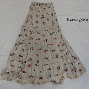 May include: A tiered maxi skirt in a light beige fabric with a fine brown pinstripe pattern and a scattered floral print in red, orange, and blue. The skirt features an elasticized waistband and a hem finished with a light brown trim. Text reads Brown Color.