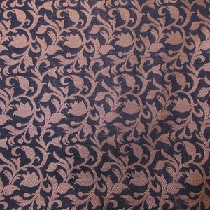 May include: Close-up of a fabric with a repeating floral pattern. The design features stylized flowers and leaves in a light brown color against a dark blue background. The fabric has a textured appearance.