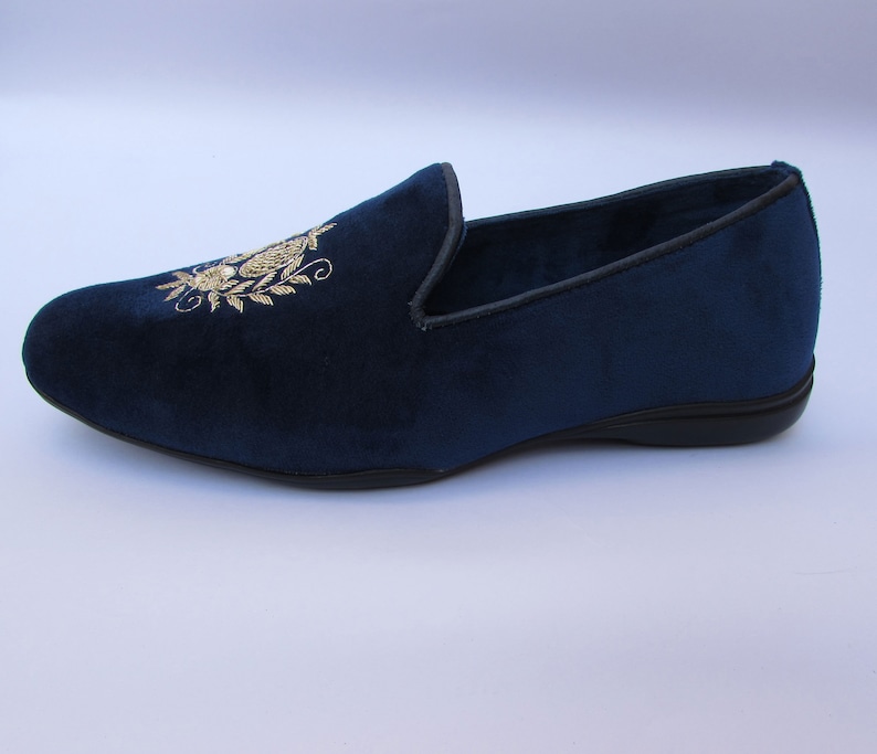 Pode incluir: Um mocassim de veludo azul-marinho com um motivo floral bordado a fio dourado no peito do p&eacute;. O sapato apresenta uma biqueira arredondada, uma silhueta de perfil baixo e uma sola preta com um rebordo fino preto ao longo da abertura do sapato.