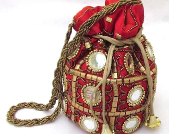 Puede incluir: Un bolso rojo con cordón, adornos dorados y un asa de cuentas. El bolso presenta detalles de espejo y un cierre de cordón dorado. El bolso mide aproximadamente 18 cm de alto y 15 cm de ancho.