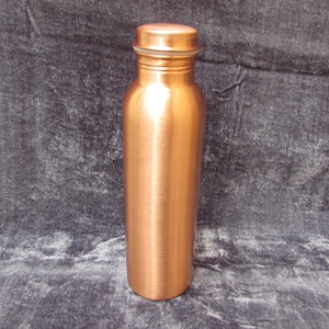 May include: A copper water bottle with a screw-on lid. The bottle has a cylindrical shape and a polished finish. The lid is the same color as the bottle. The bottle is approximately 9 inches tall.