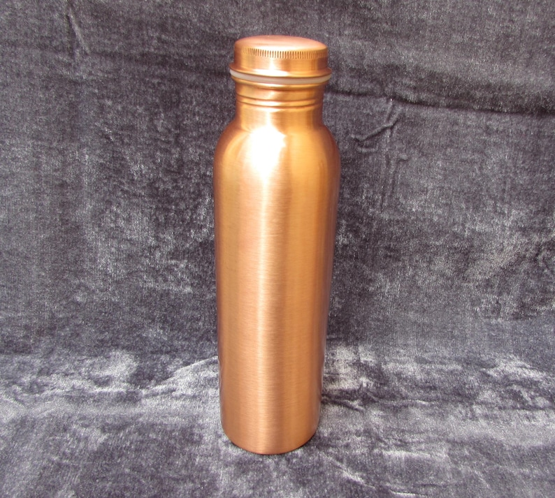 May include: A copper water bottle with a screw-on lid. The bottle has a cylindrical shape and a polished finish. The lid is the same color as the bottle. The bottle is approximately 9 inches tall.